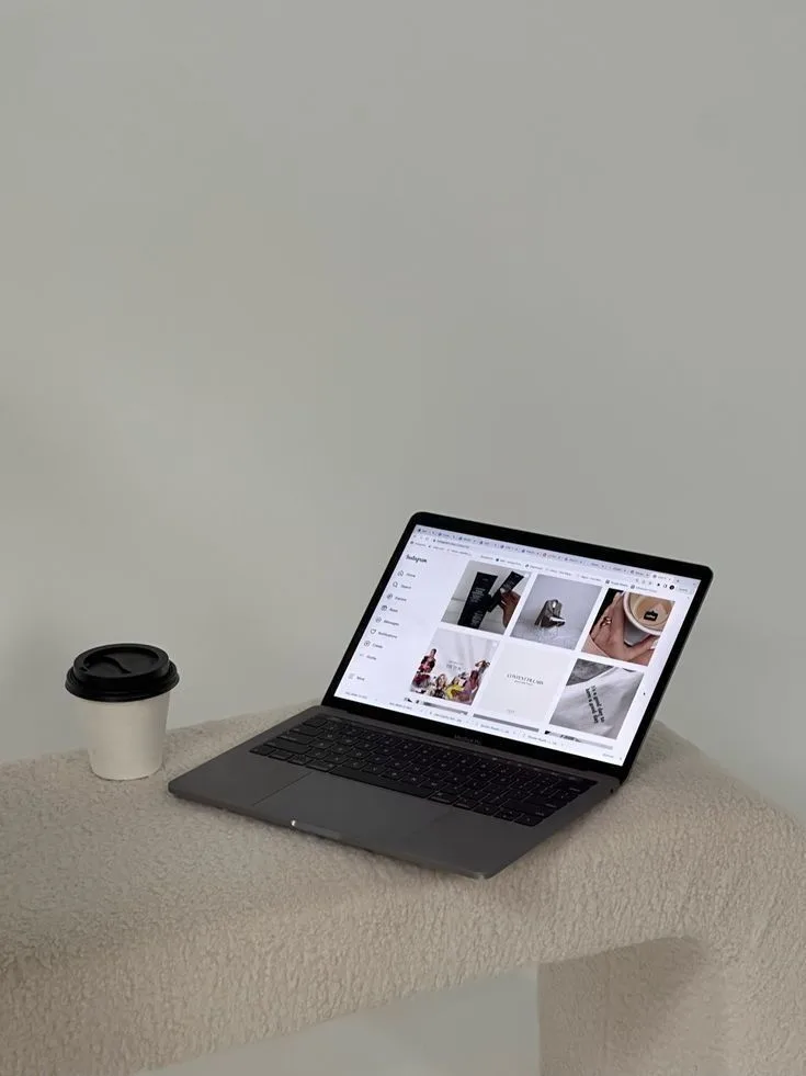 A laptop open on a consistent Instagram grid beside a takeaway coffee