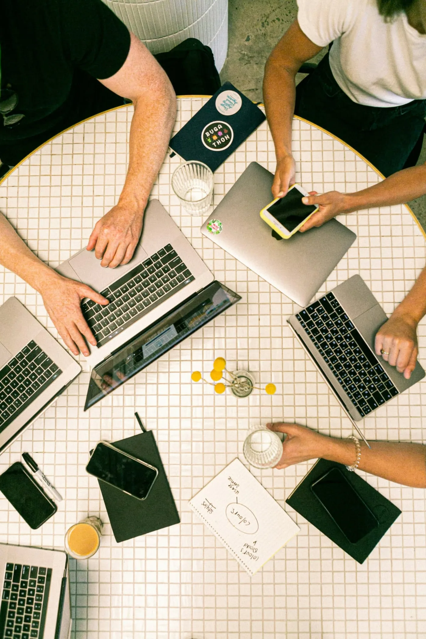 A team around a tiled table with laptops, phones and a notebook, working through a brief